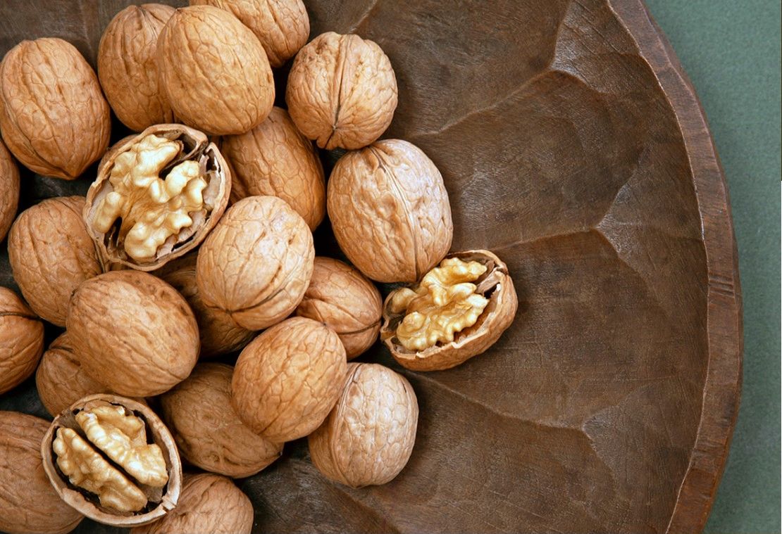 Inshell and cracked Chandler walnuts in a wooden bowl